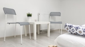 A bedroom with a bed, a bedside table, two chairs, a radiator, and a potted plant. - Visit Lublin Apartments Piłsudskiego (Lublin)