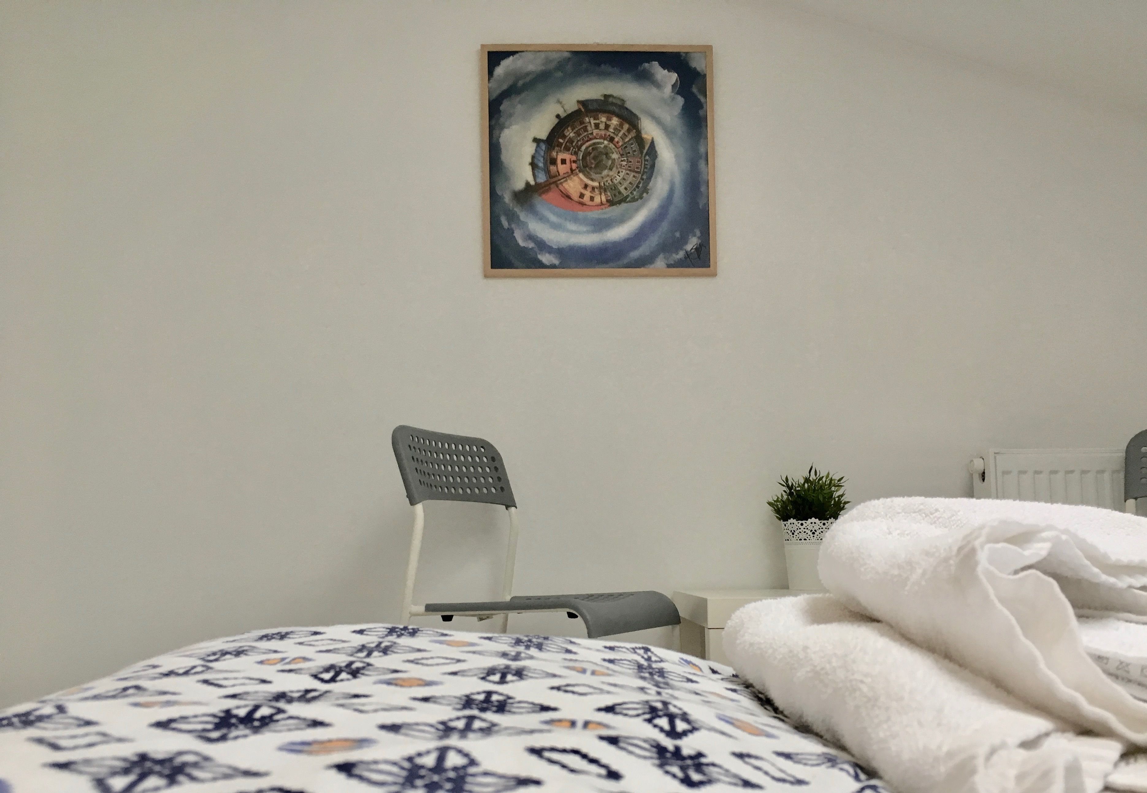 A bedroom with a bed, a chair, a radiator, and a small plant.