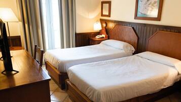 A hotel room with two beds, a desk, a lamp, a telephone, and a framed picture on the wall.