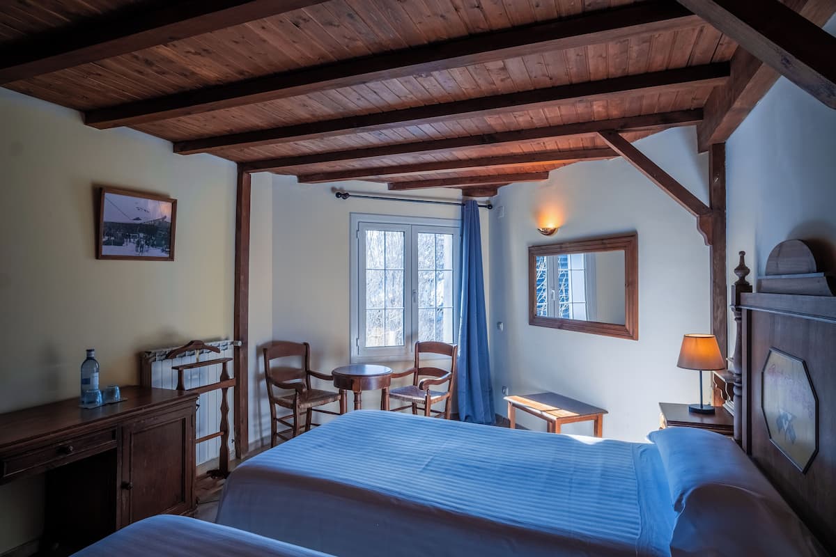 Habitación de hotel con techo de madera, cama, escritorio, silla, mesita, lámpara y ventana con cortinas.