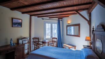 Habitación de hotel con techo de madera, cama, escritorio, silla, mesita, lámpara y ventana con cortinas.
