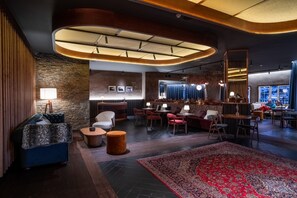 A modern lounge area with a stone wall, a large red patterned rug, and a mix of seating options including sofas and chairs. - The Mountains Hotel (Monachil)