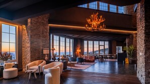 A spacious lobby with stone walls, large windows, and a chandelier. - The Mountains Hotel (Monachil)