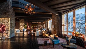 A spacious lobby with stone walls, modern furniture, and large windows offering a view of a snowy landscape. - The Mountains Hotel (Monachil)
