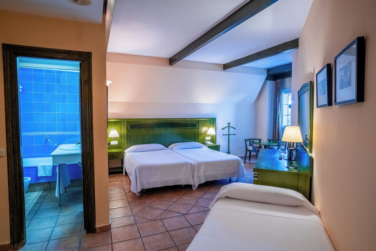 Una habitación de hotel con dos camas, baño, escritorio y una silla.