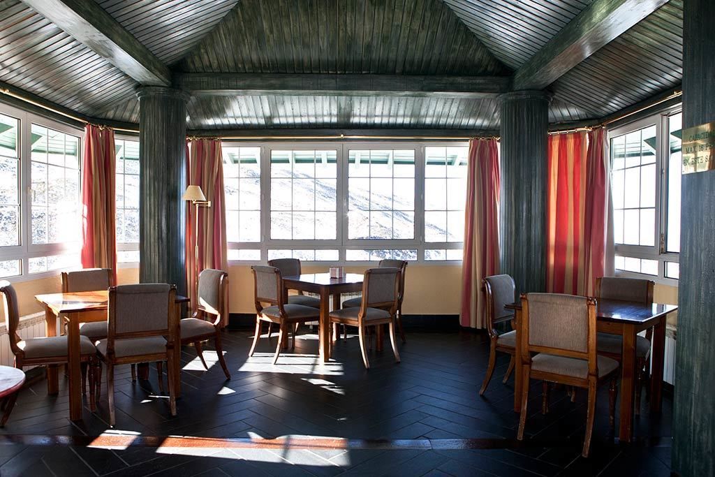 A room with a wooden ceiling, large windows with curtains, and a central table with chairs.