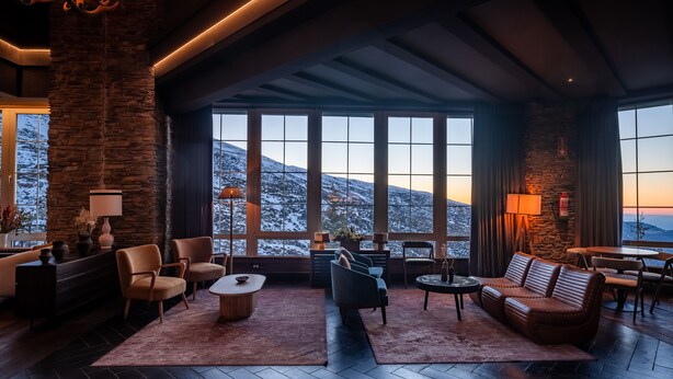 A spacious living area with large windows, a stone accent wall, and modern furniture. - The Mountains Hotel (Monachil)