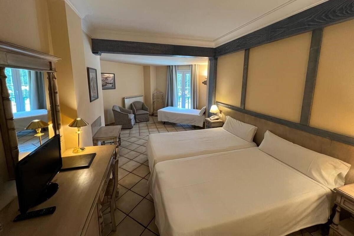 Habitación de hotel con dos camas, un escritorio, una silla, una lámpara y una ventana con cortinas.