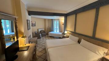 Habitación de hotel con dos camas, un escritorio, una silla, una lámpara y una ventana con cortinas.