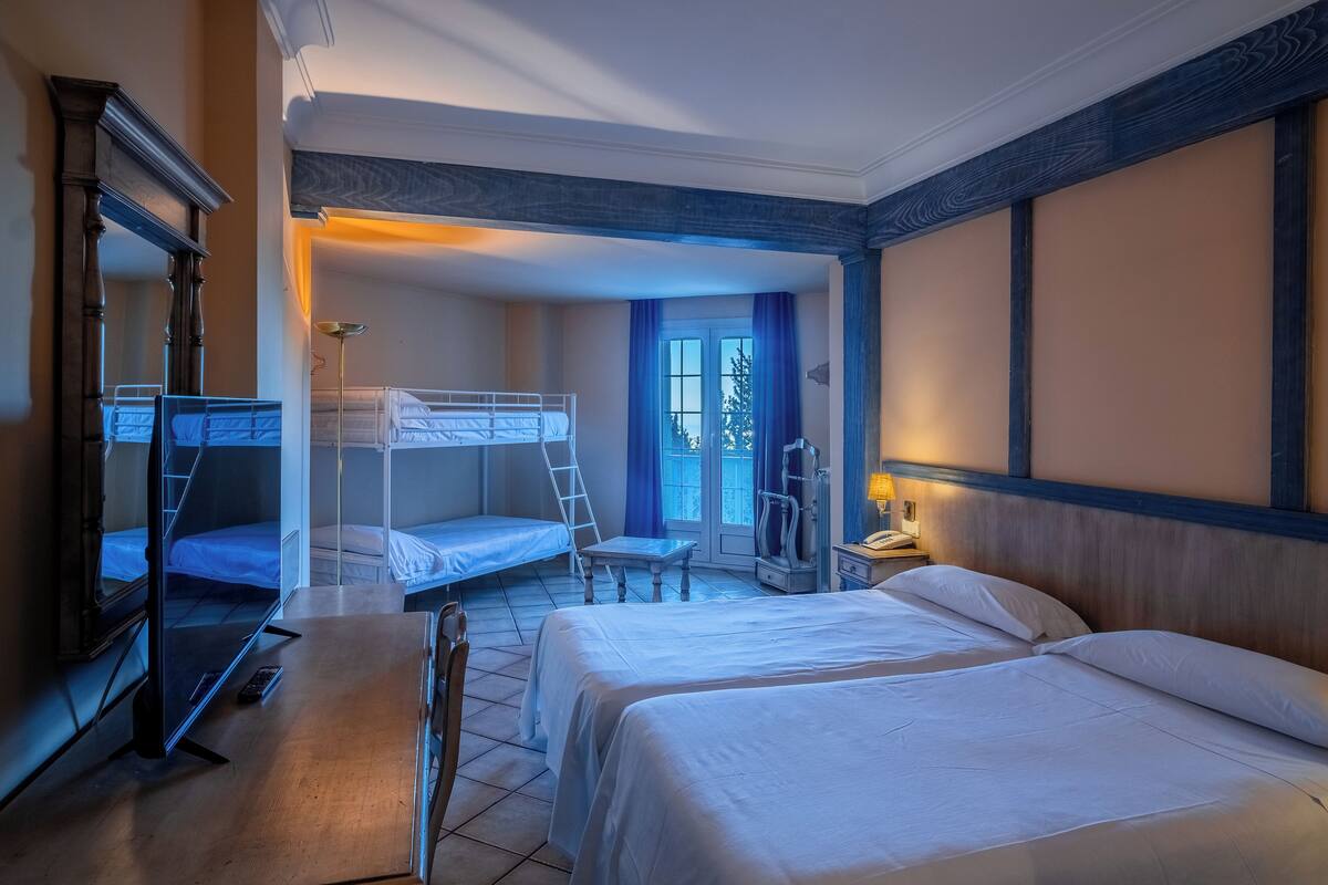 Habitación de hotel con literas, un escritorio, una silla, un televisor y una mesita de noche.