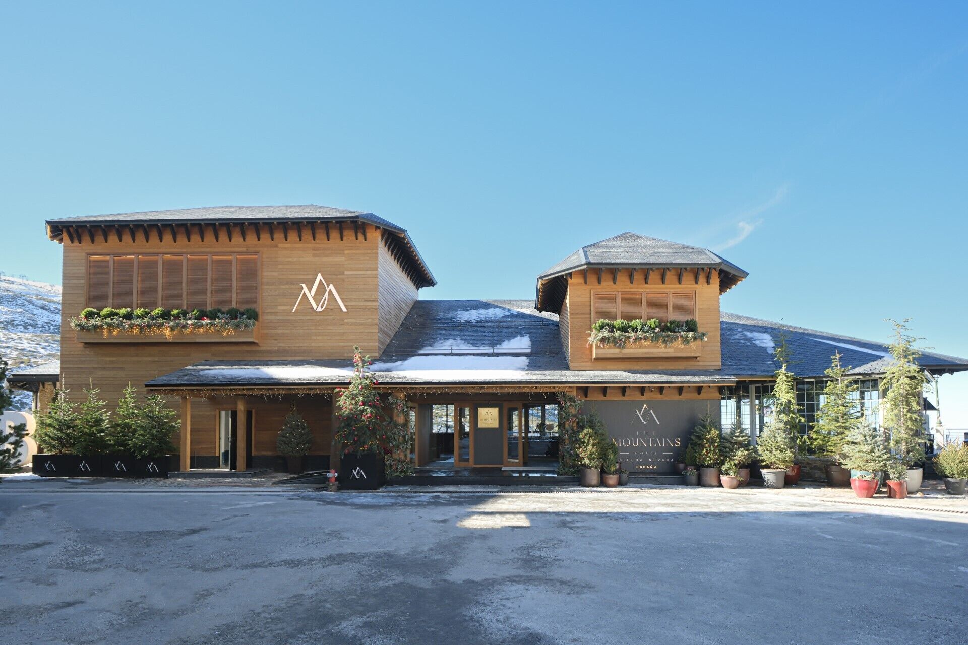 A hotel with a wooden facade, two distinct sections, and potted plants on the roof.