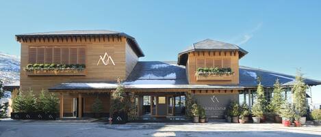 A hotel with a wooden facade, two distinct sections, and potted plants on the roof.