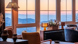 A room with large windows, a wooden table, a chair, a lamp, and a view of mountains. - The Mountains Hotel (Monachil)
