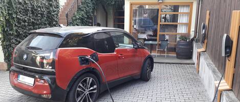 A red BMW i3 charging in a courtyard with a brick floor, a wooden fence, and a building with a glass door in the background.