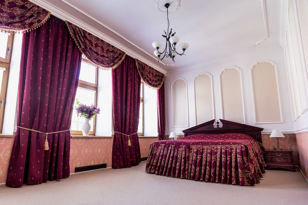 Ein Schlafzimmer mit einem großen Bett, einer Chandelier und einem fenster mit Vorhängen.