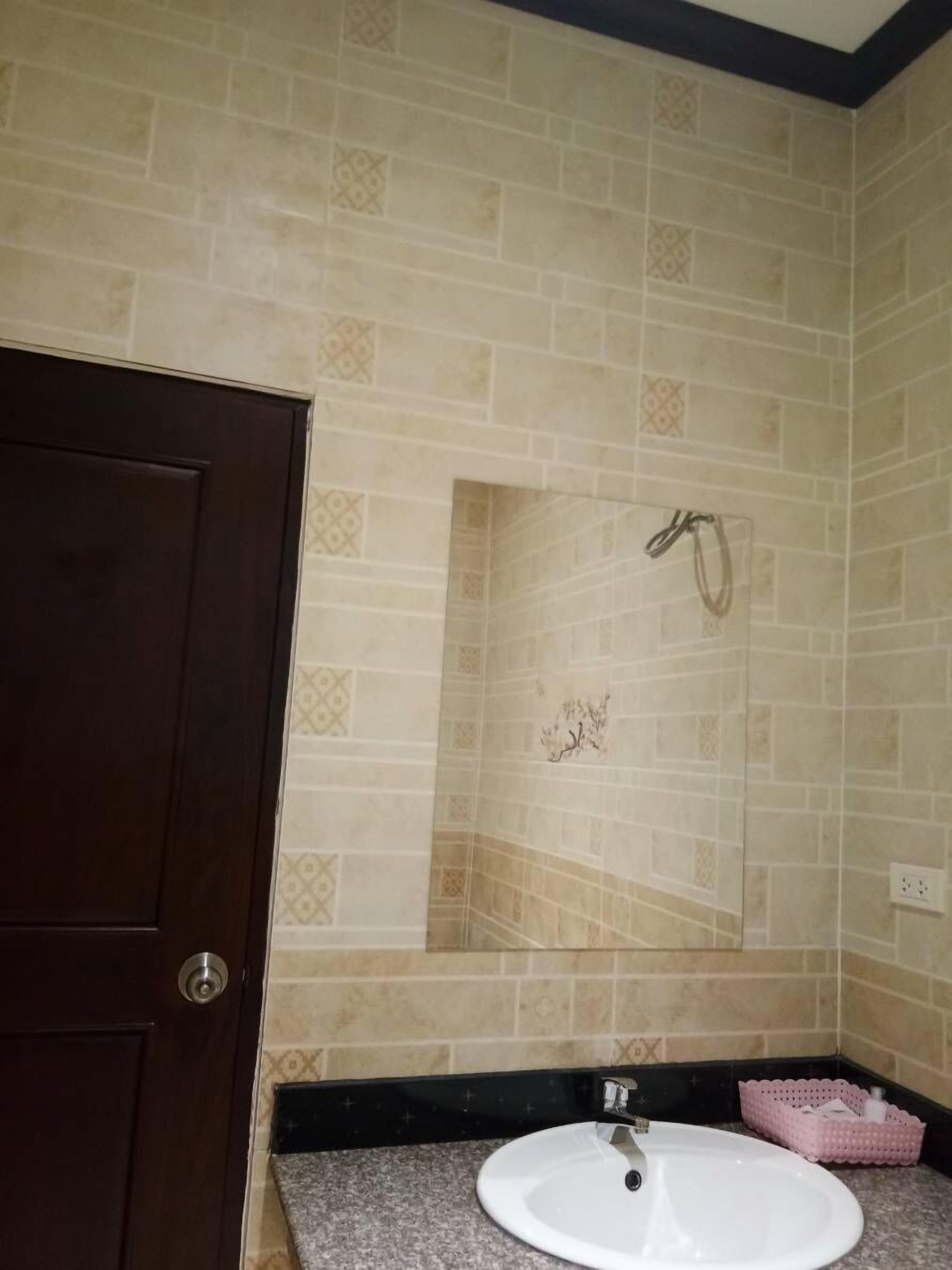 A bathroom with beige patterned tiles, a white sink, a dark wooden door, and a shower area with a towel rack.