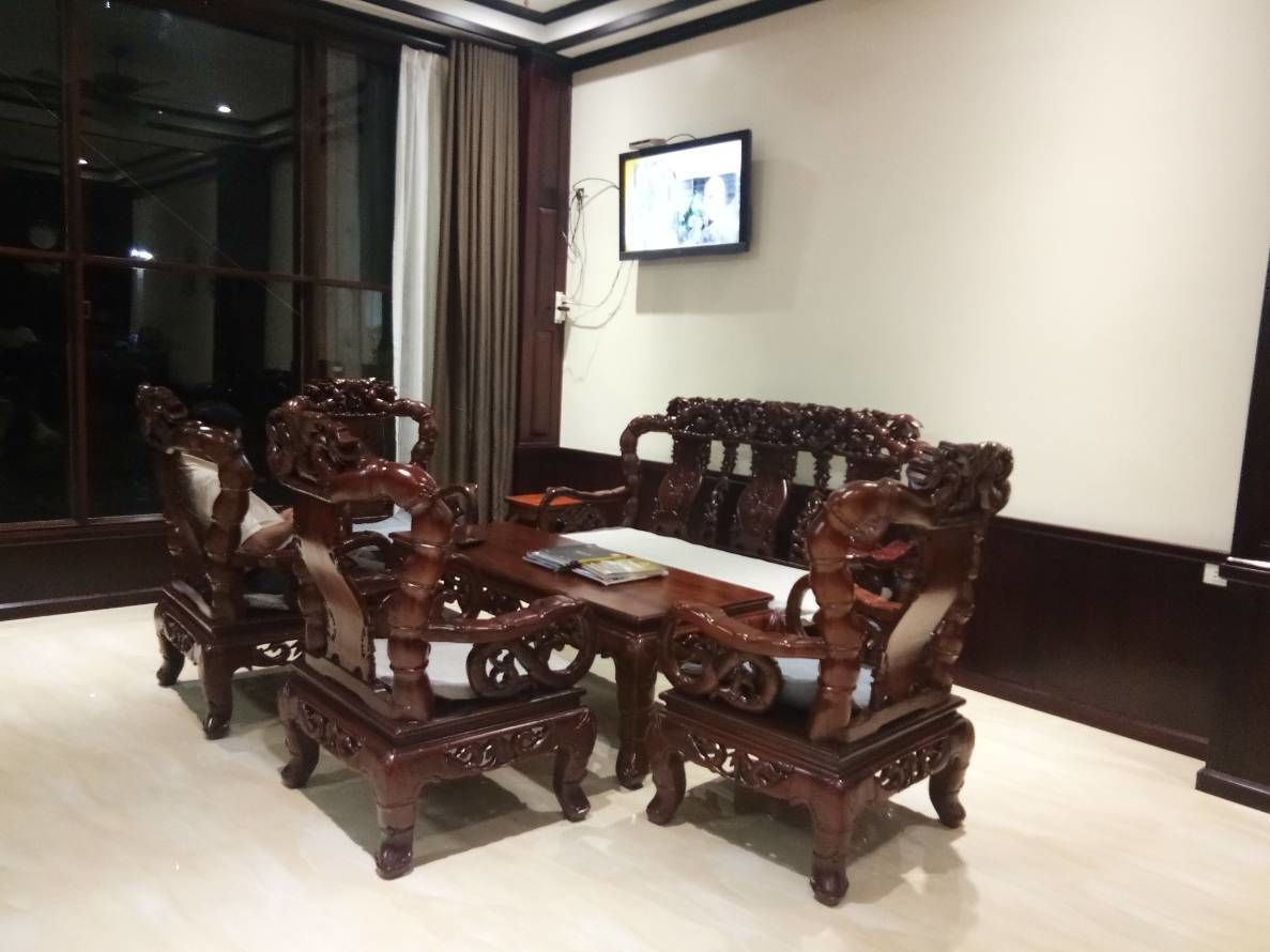 A traditional wooden sofa set with intricate carvings, a matching coffee table, and a television mounted on the wall.