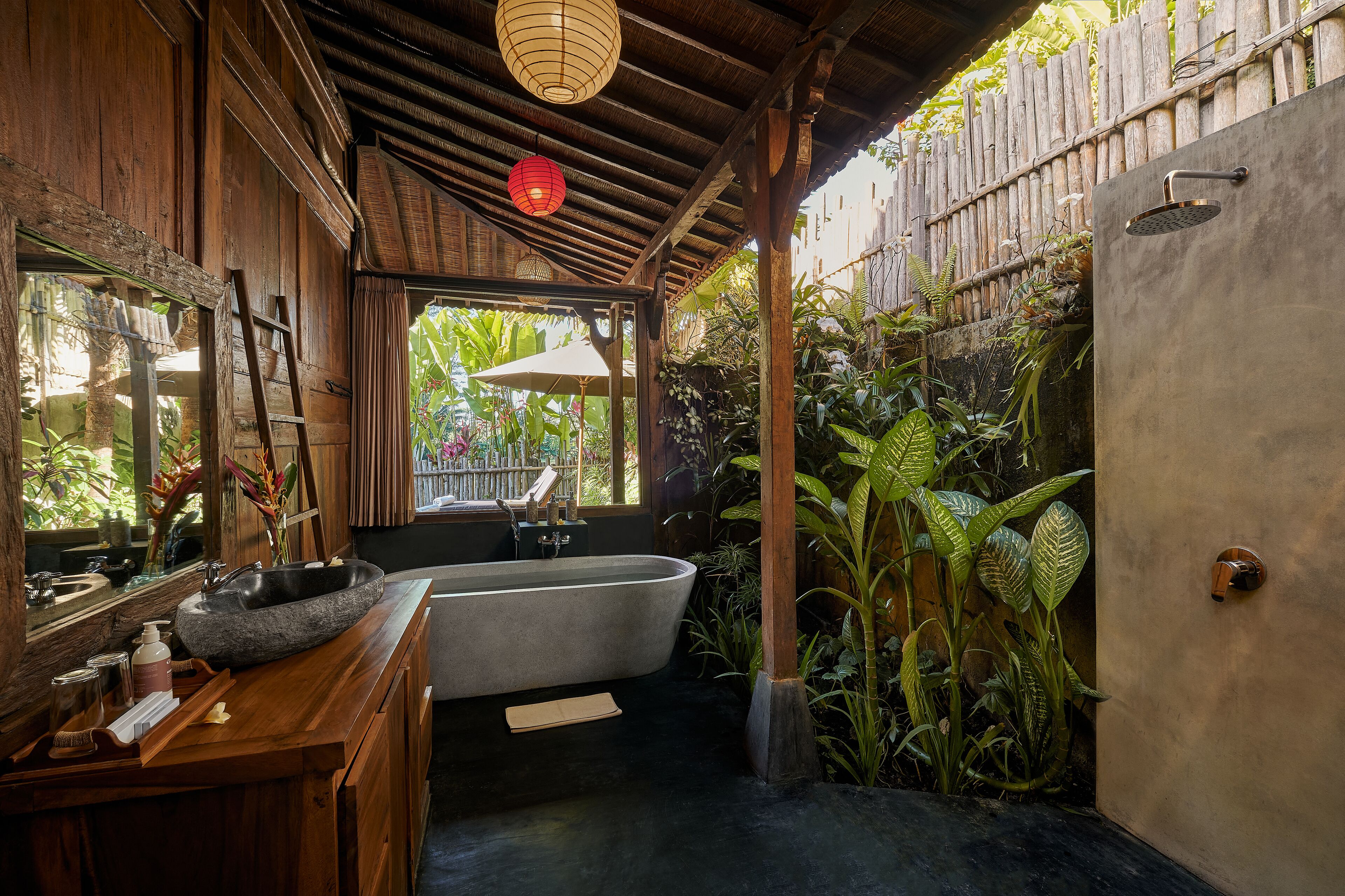 A bathroom with a freestanding bathtub, wooden vanity, and a large window with a view of tropical plants.
