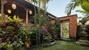 Edificio in legno tradizionale con ingresso in mattoni, immerso in piante tropicali rigogliose e un vialetto in pietra.