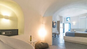 A modern, minimalist living room with a sofa, a small table with a wine bottle, and a lamp. - Euphoria Suites (Santorini)