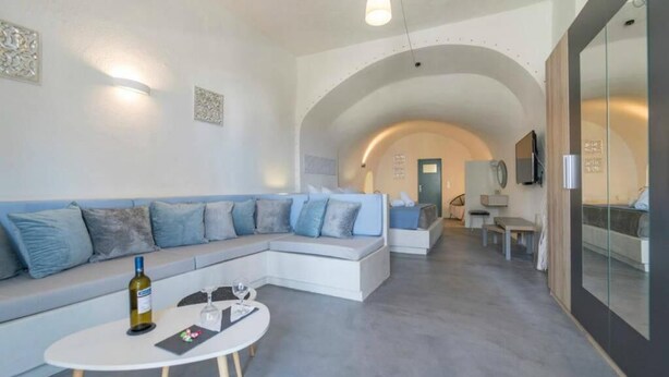 A modern living room with a sectional sofa, a round coffee table, and a television. - Euphoria Suites (Santorini)