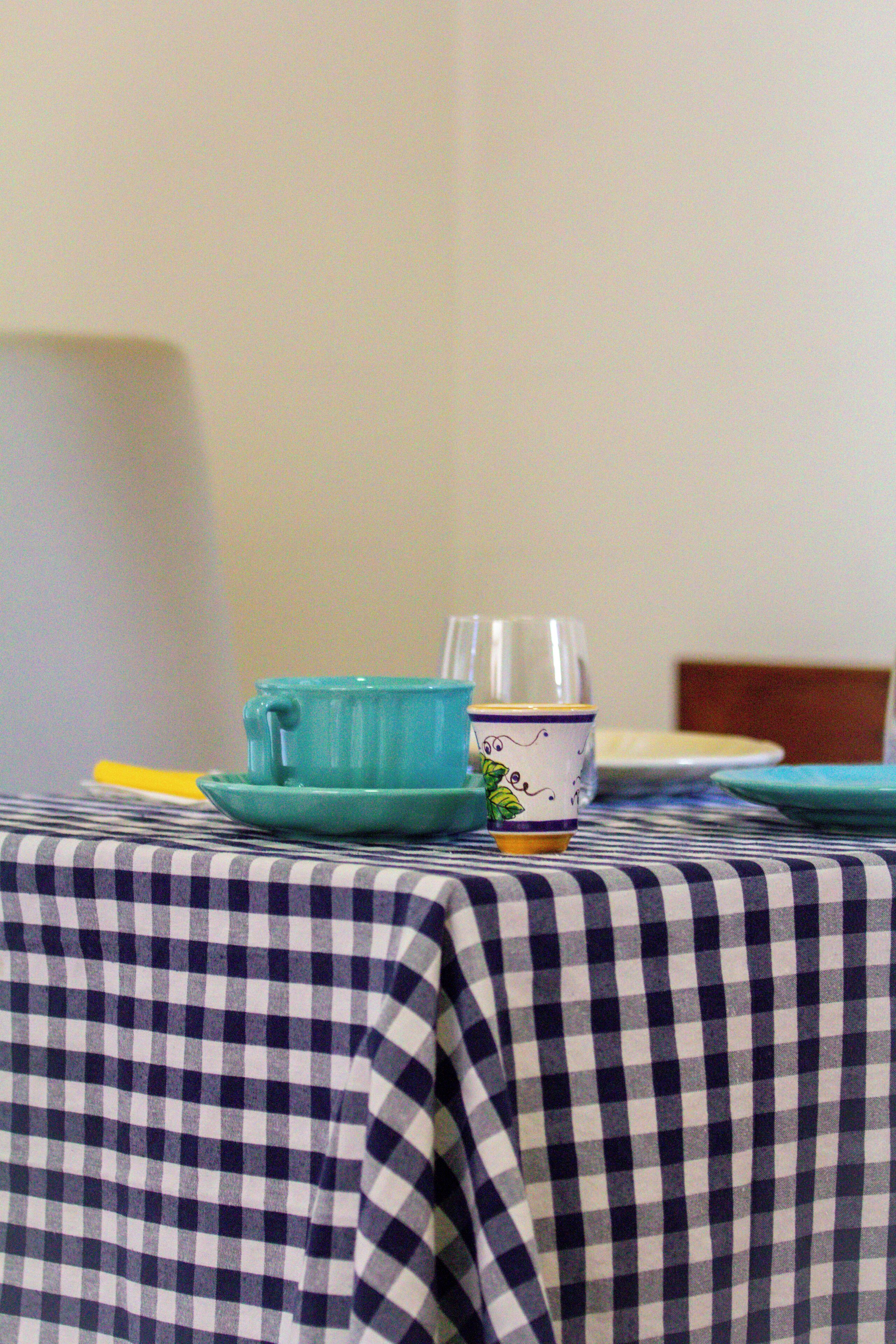 Une nappe à carreaux, une tasse et une soucoupe bleues, une assiette blanche et un verre, le tout posé sur une table.