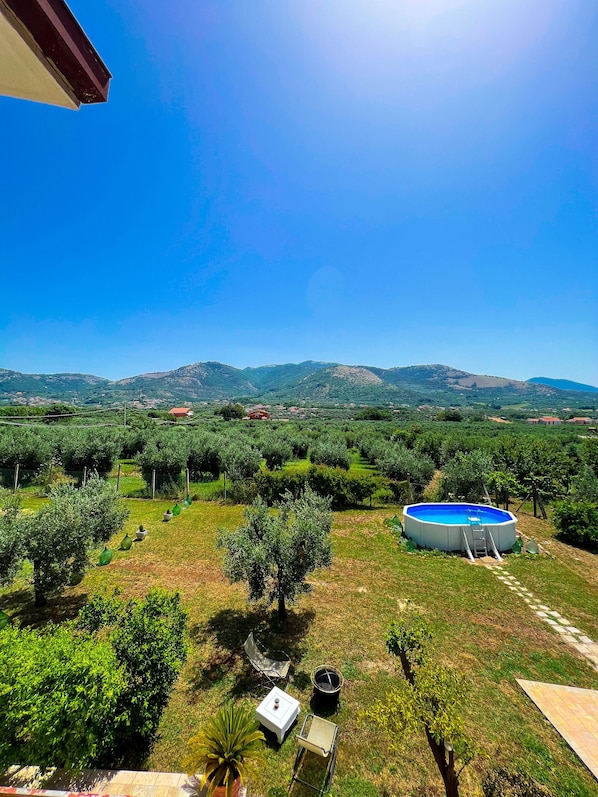 An outdoor area with a swimming pool, a table, and chairs, surrounded by greenery and hills in the background. - Bed and Breakfast Nero Buono (Cori)