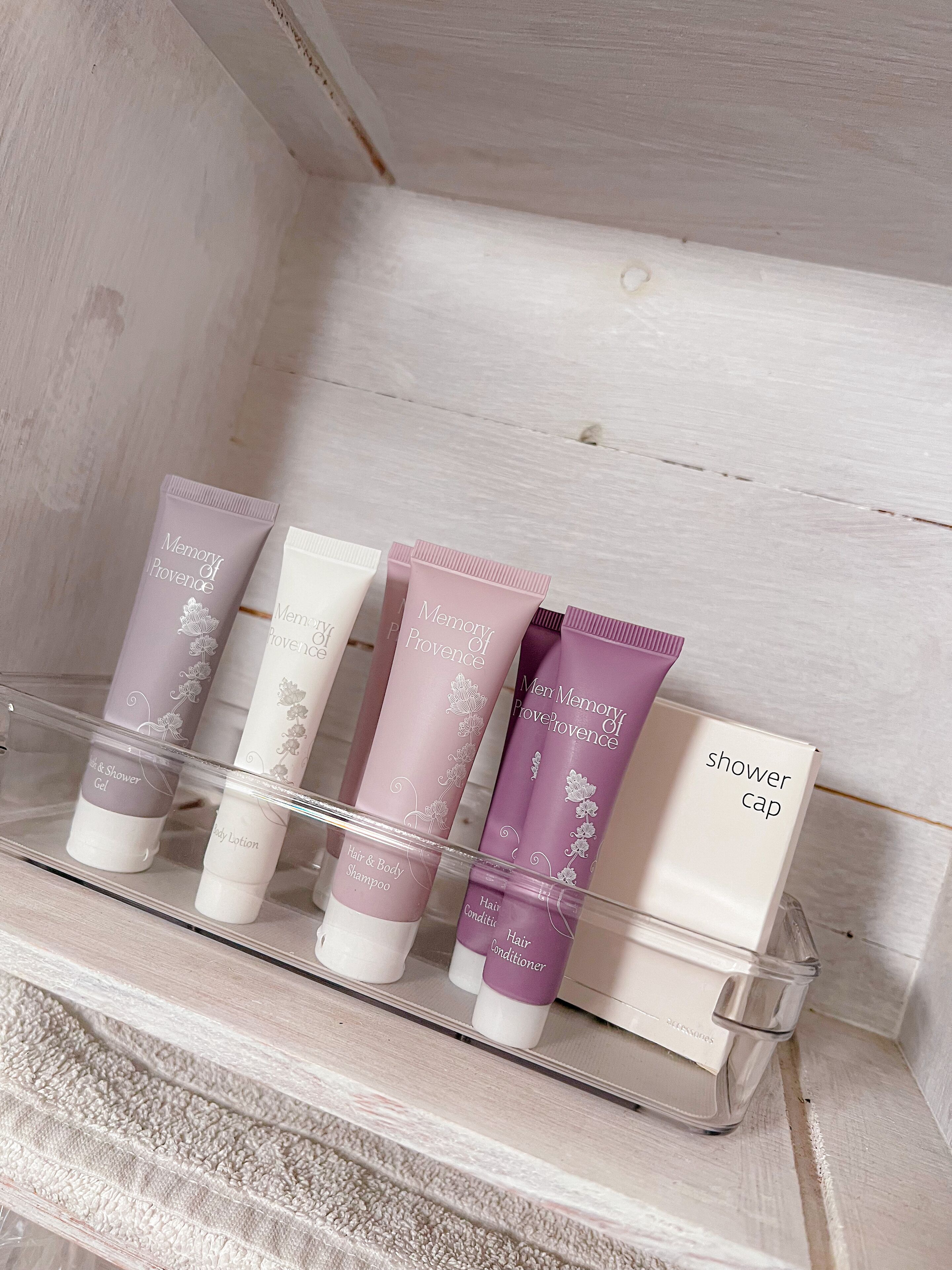 A bathroom shelf with various toiletries including a shower cap, hair conditioner, body lotion, and hair & body shampoo.