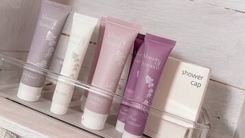 En badeværelseshylde med forskellige toiletartikler, heriblandt badehue, hårkur, bodylotion og shampoo til hår og krop.