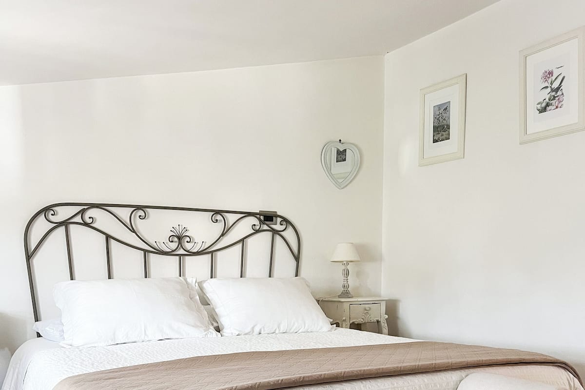 Een slaapkamer met een bed, een nachtkastje, een lamp en een spiegel in de vorm van een hart aan de muur.