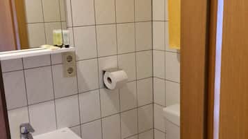 A bathroom with a white sink, a mirror, a toilet, and a roll of toilet paper on the wall.