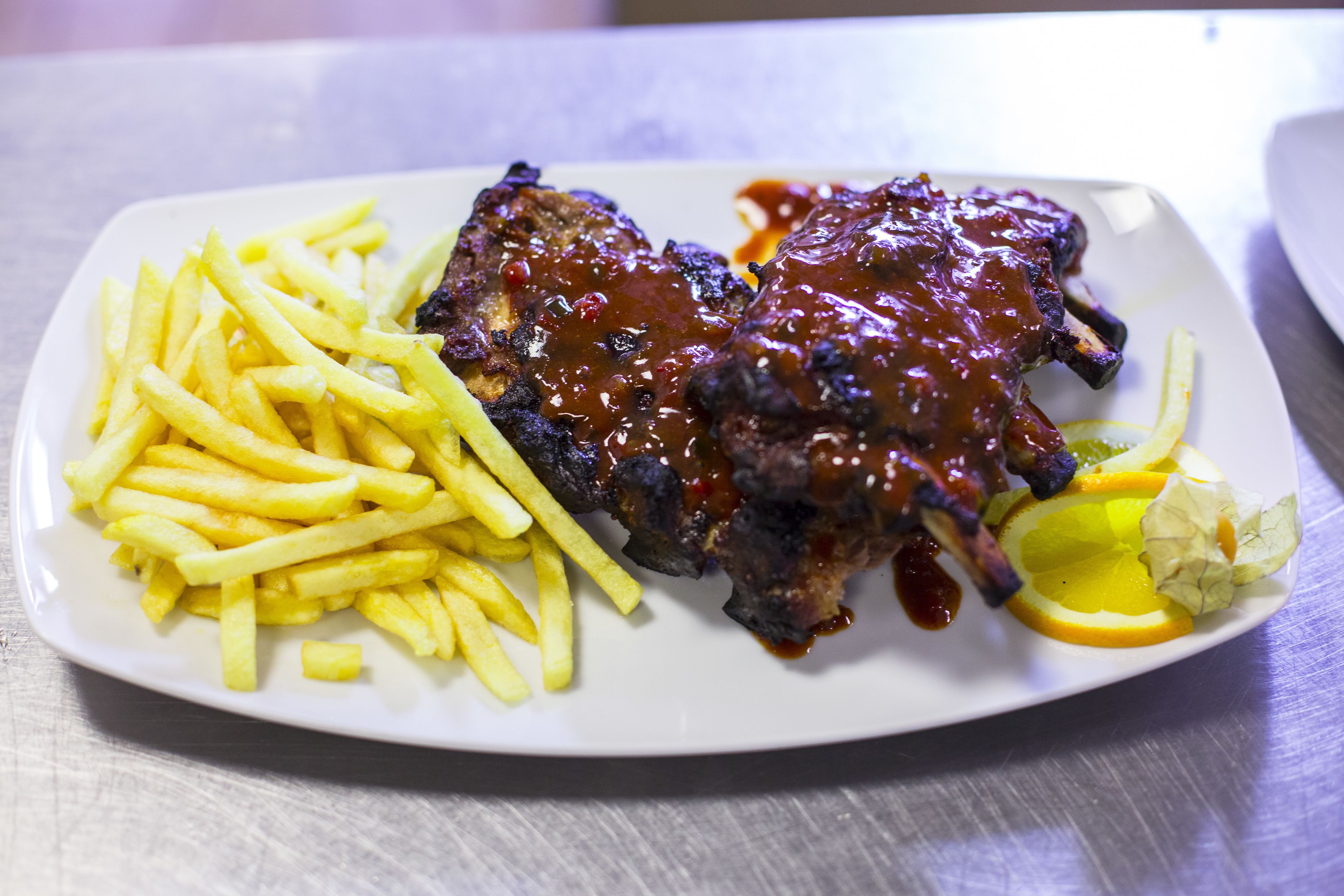 Ein Teller mit Rippchen, Barbecue-Sauce, Pommes Frites und einem Zitronenschnitz.