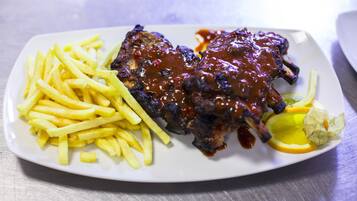 Ein Teller mit Rippchen, Barbecue-Sauce, Pommes Frites und einem Zitronenschnitz.