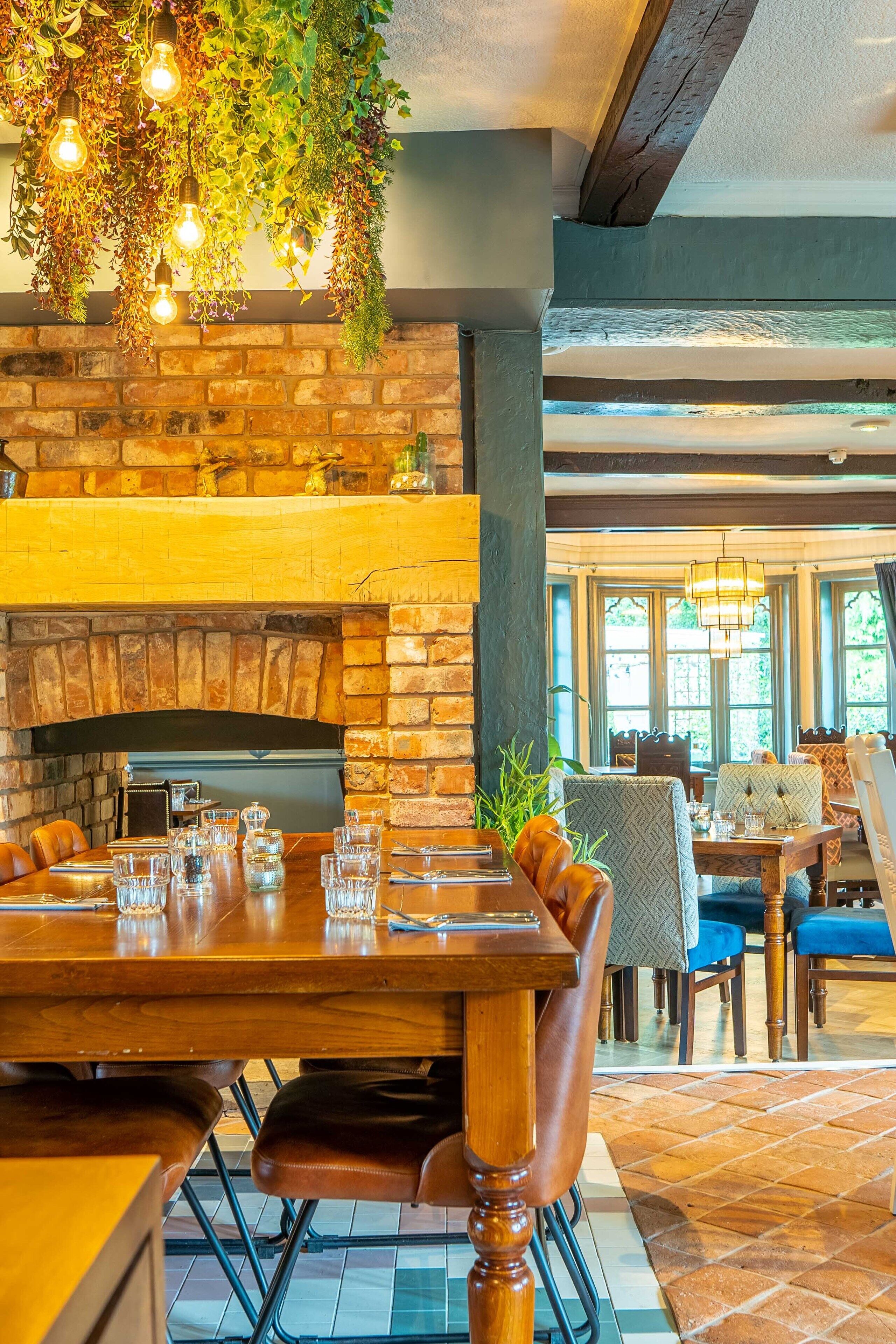 Un restaurante con chimenea de ladrillo, una mesa de comedor de madera y lámparas colgantes.