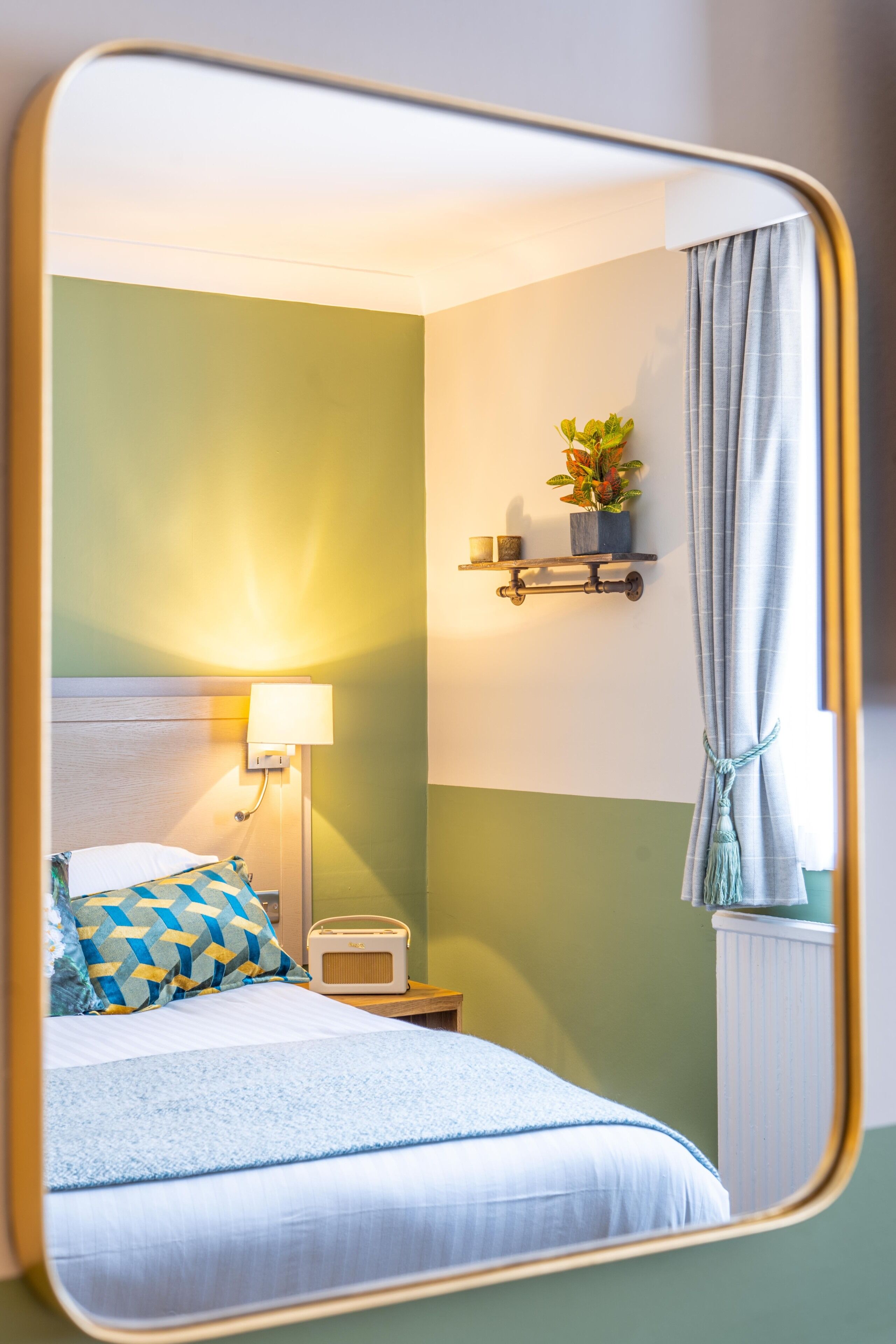 Quarto de hotel com cama, abajur, rádio e prateleira com uma planta.
