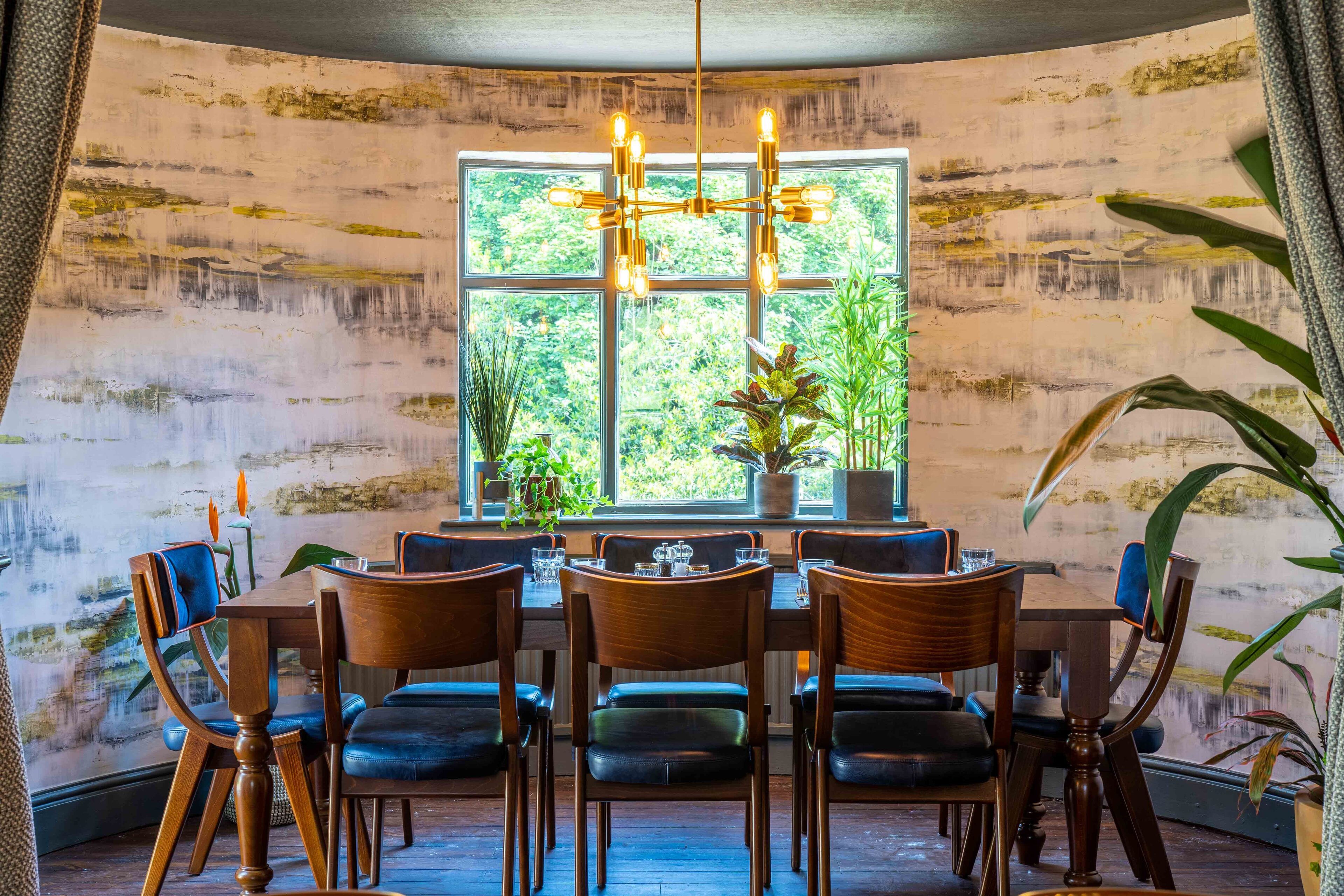 A dining area with a large window, wooden chairs, and a chandelier.