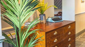 Une commode en bois avec de nombreux tiroirs, un tableau encadré, une machine à écrire et une plante en pot.
