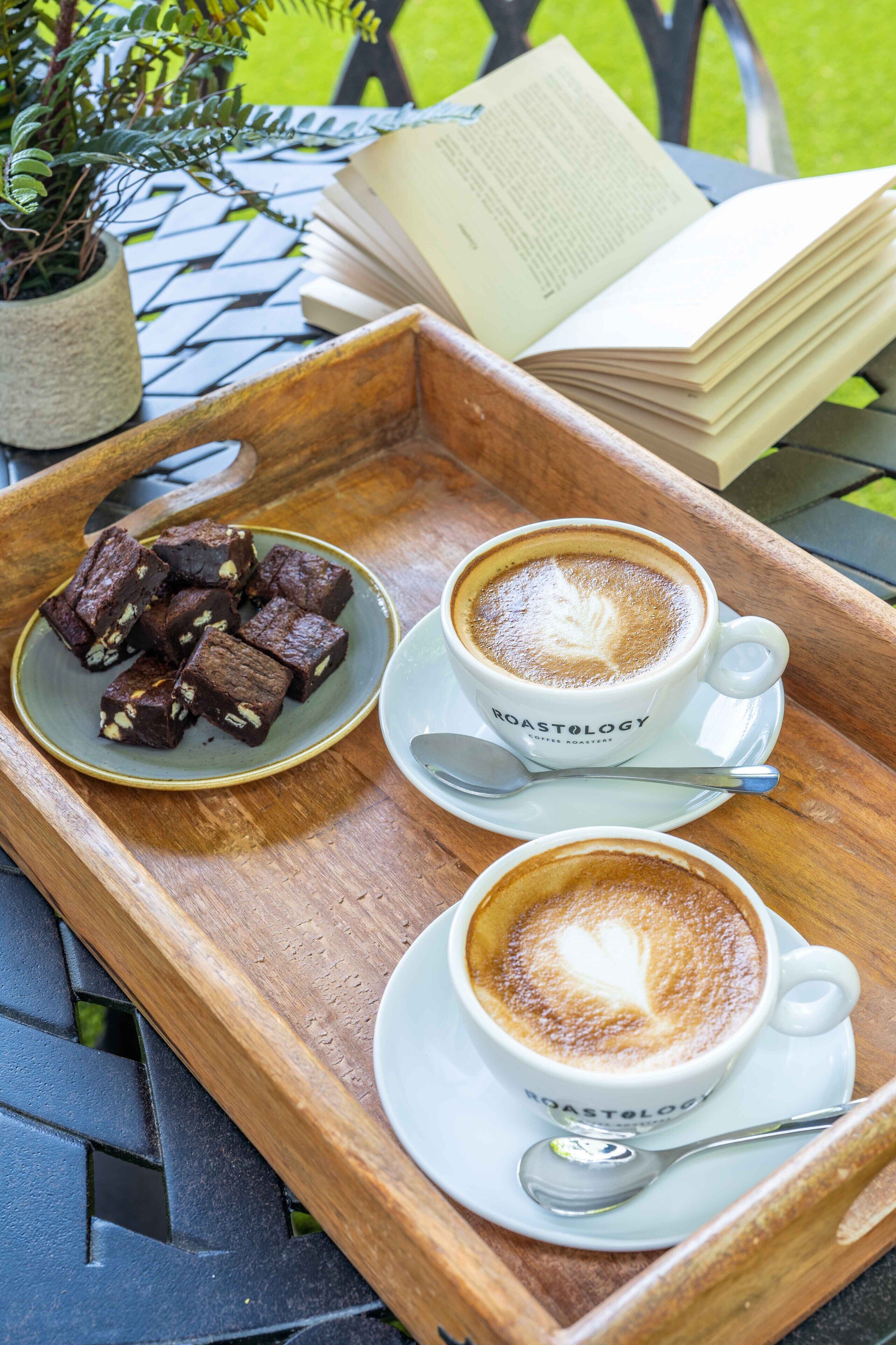 Un plateau avec deux tasses de café et un bol de brownies, posé sur une table en bois.