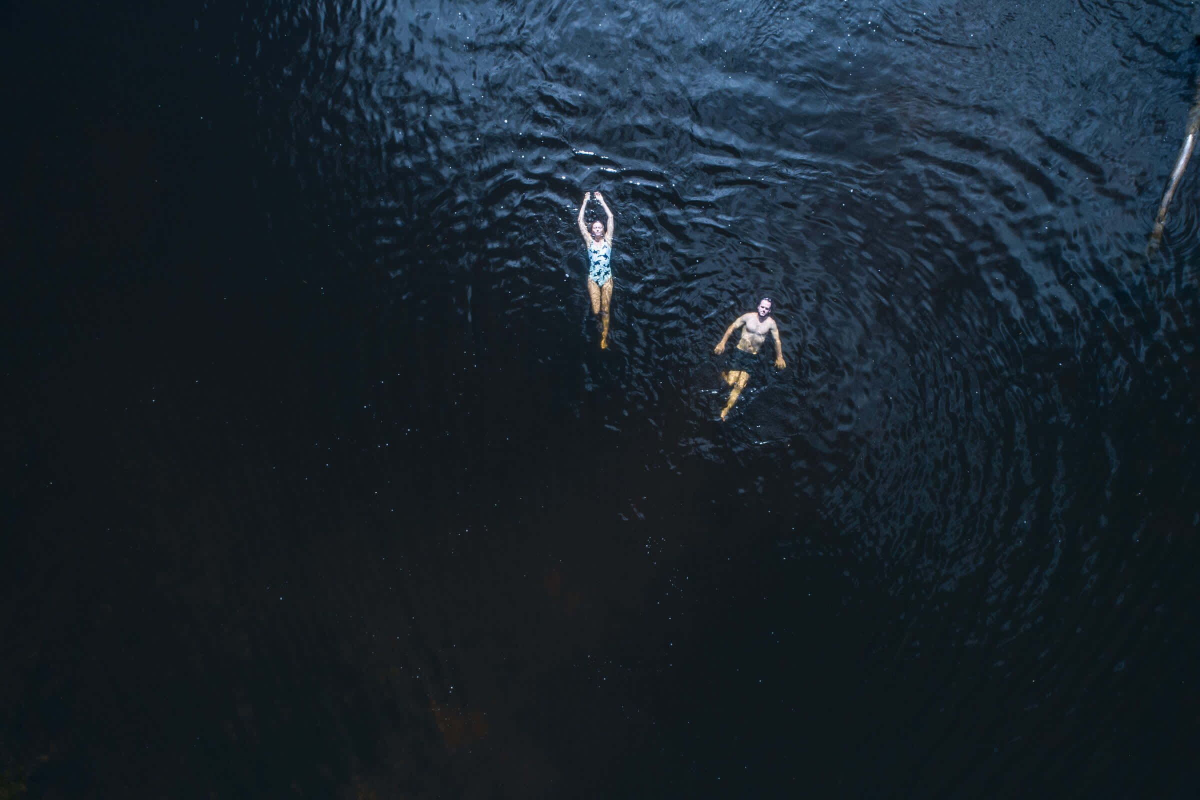 Dos personas nadando en aguas oscuras.