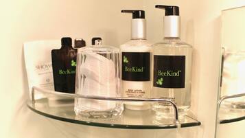 Una repisa de vidrio con tres botellas de loción corporal BeeKind y una botella de vidrio transparente con bomba.