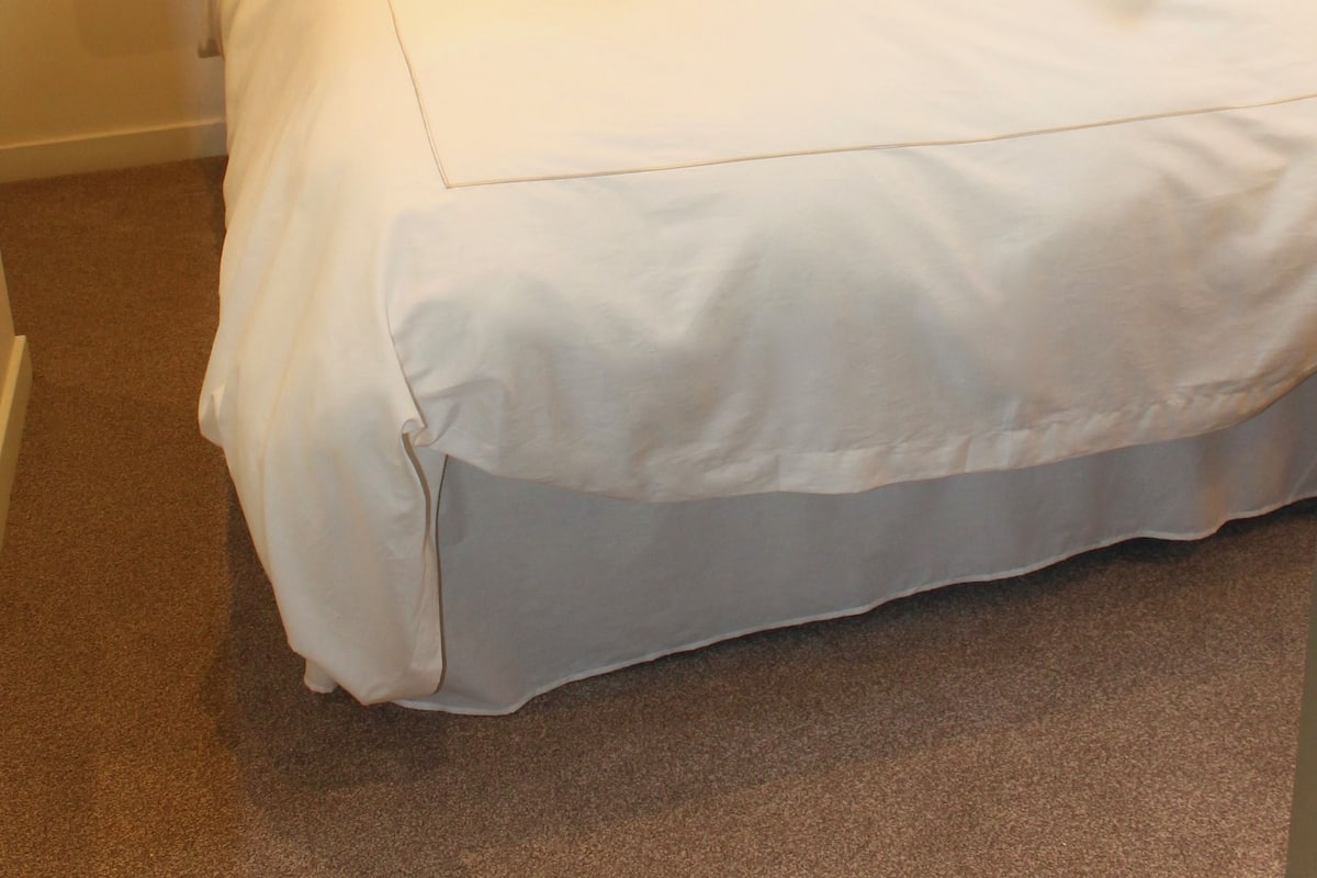 A neatly made bed with white linens and a decorative pillow, a wooden headboard, and bedside lamps.