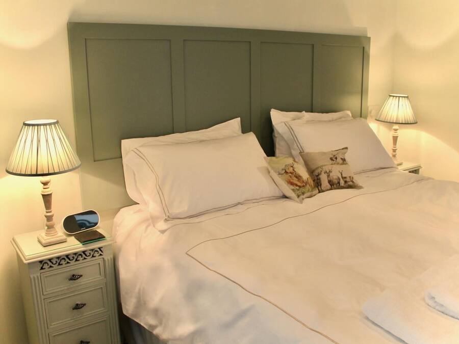 A neatly made bed with white linens, two bedside lamps, and a small bedside table with a lamp and a smartphone.