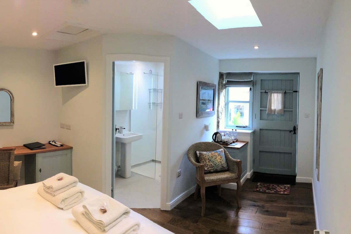 A hotel room with a bed, a desk, a chair, a TV, a bathroom, and a view of the outside.