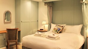 Ein ordentlich bezogenes Bett mit Kissen und gefalteten Handtüchern, ein Nachttisch mit Lampe, ein Sessel und ein Kleiderschrank in einem Hotelzimmer.
