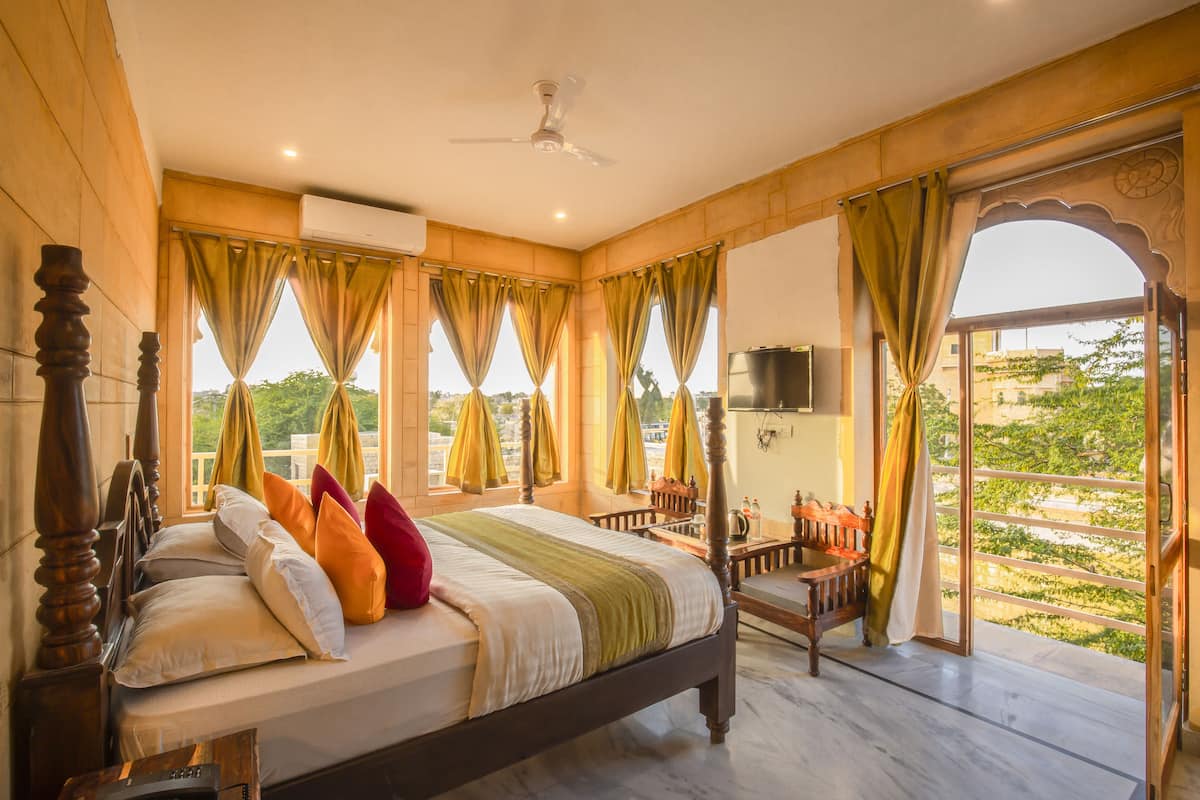 A bedroom with a large bed, curtains, a ceiling fan, and a view of greenery outside.