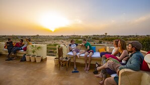 A group of people sitting on outdoor furniture on a terrace with a sunset view. - Boutique Helsinki (Jaisalmer)