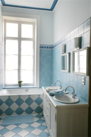 Ein Badezimmer mit Fenster, zwei Waschbecken, einer Badewanne und einer kleinen Pflanze.