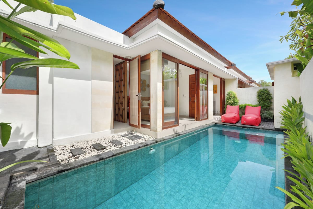 A modern house with a swimming pool, red chairs, and a garden.