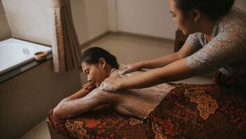 A person receiving a massage in a room with a bathtub and a window.