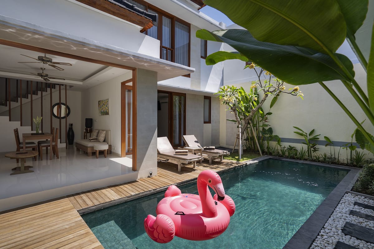 A modern house with a swimming pool, a wooden deck, and a pink flamingo float.